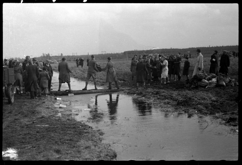 Operatie Manna. Vrijwilligers geven voedselpakketten aan elkaar door over een stuk hout in een sloot. De pakketten zijn daar gedropt door geallieerde vliegtuigen voor de hongerige bevolking van Rotterdam e.o.