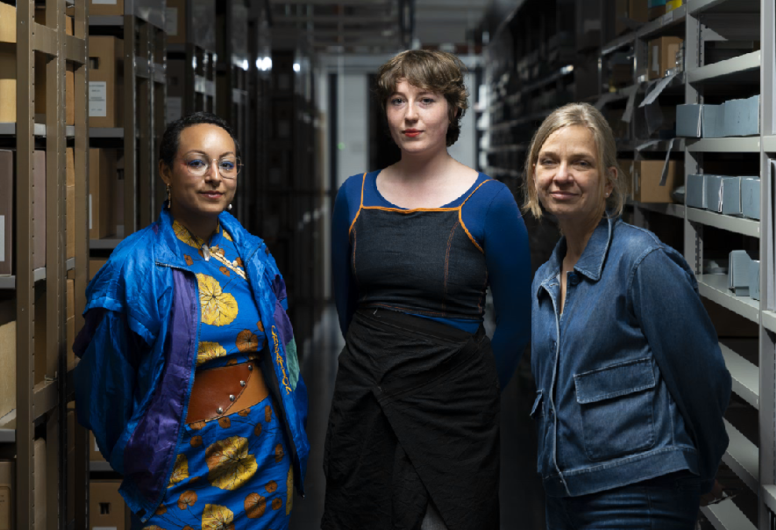 3 dames poseren naast elkaar in een archiefdepot met weinig verlichting