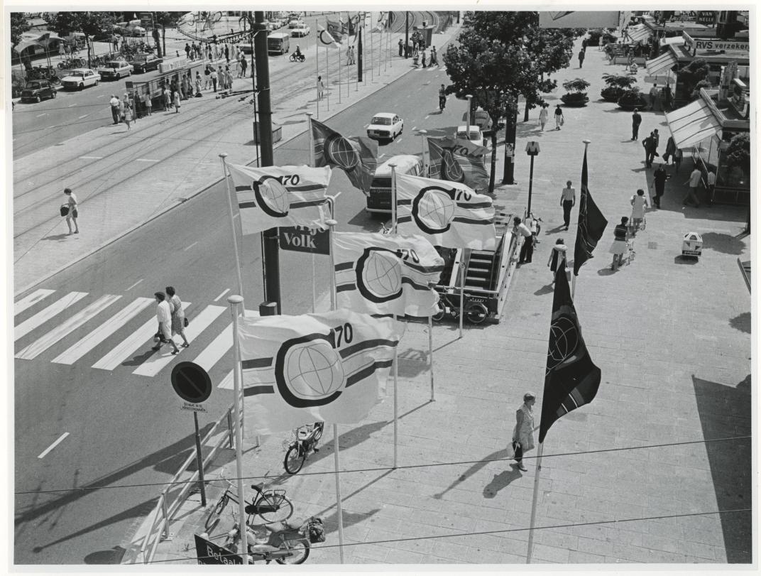 Blik vanuit de kabelbaan op de Coolsingel in zuidelijke richting met vlaggen met het logo van de Manifestatie C70. Fotograaf H.M. Vrijmoet. Collectie 4282, nummer 2142
