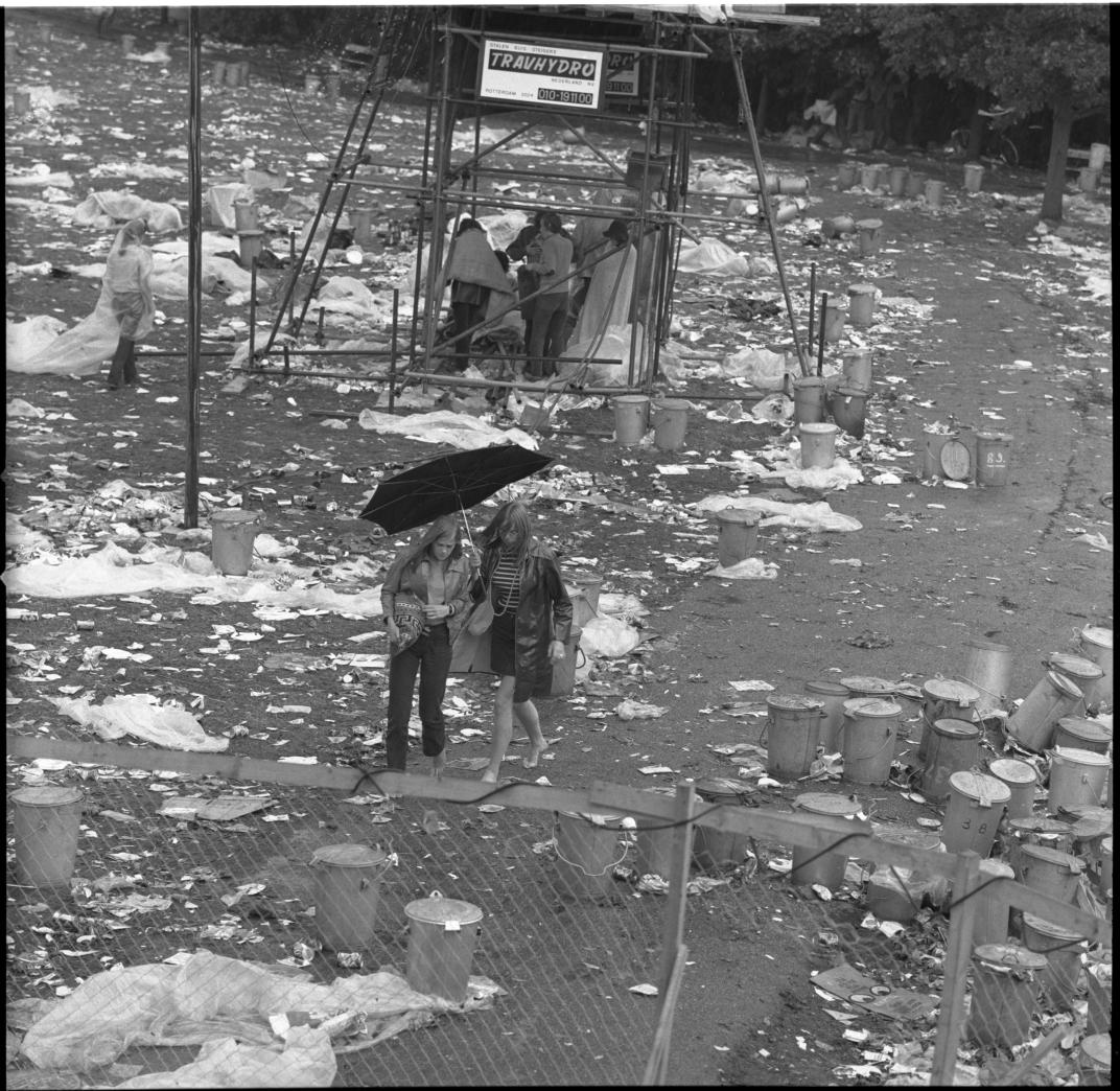 Laatste toeschouwers gaan naar huis na de afloop van het Holland Pop Festival bij de Plaszoom in het Kralingse Bos. Op de voorgrond veel afval en prullebakken.