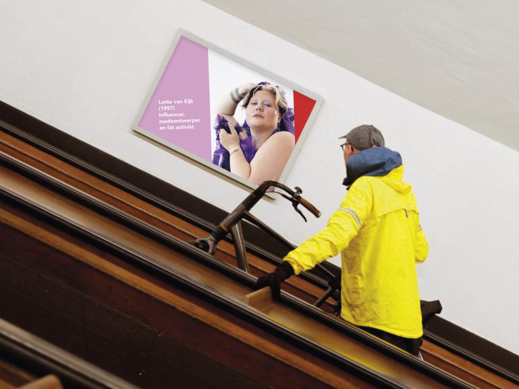 Man op fiets de roltrap op in de fietstunnel kijkend naar een afbeelding van een vrouw op de muur
