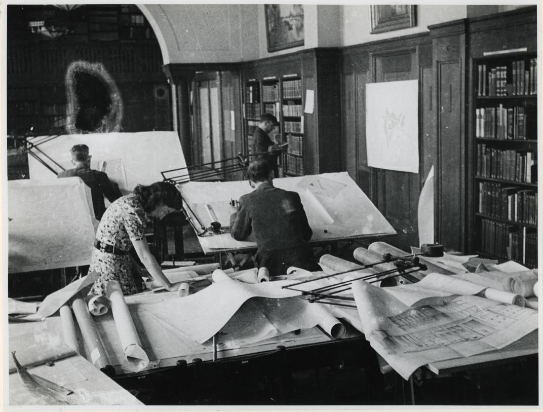 Medewerkers achter tekentafels in kantoren van het ASRO in de Gemeentebibliotheek.