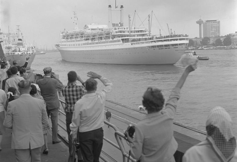 Zwaaiende mensen op de kade van de Holland Amerika-Lijn-vertrekhallen aan de Wilhelminakade. De ss Rotterdam vaart uit, 1968.  Nummer uit collectie: NL-RtSA_4121_24162-1-14