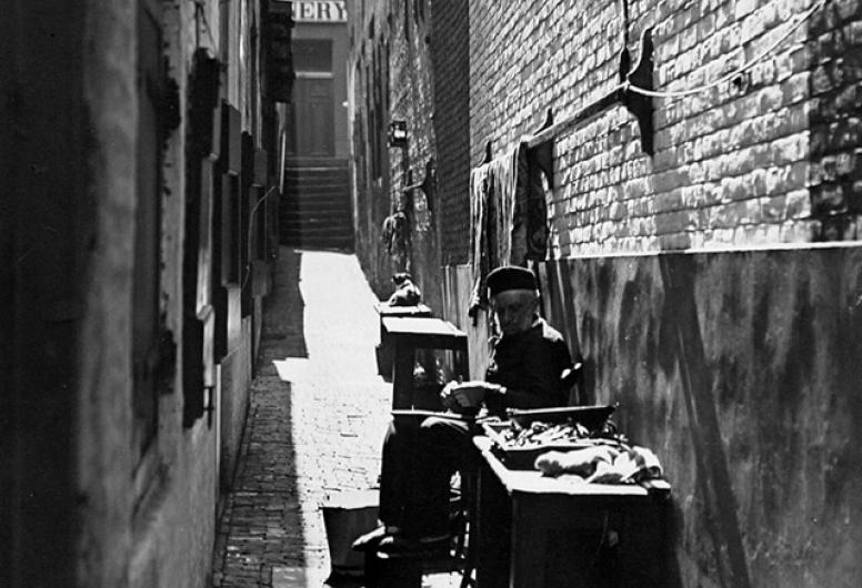 Lange steeg, met een man in het midden zittend naast ingang van het huis.