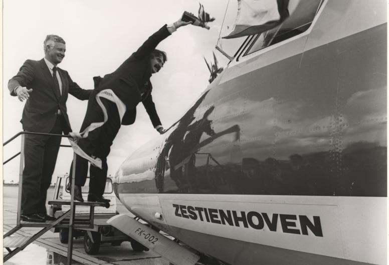 16 juni 1981: Burgemeester Van der Louw doopt met een fles champagne het nieuwe toestel van de Nederlandse Luchtvaartmaatschappij (NLM) op Zestienhoven. De directeur van NLM, A.J. Meyer, houdt een oogje in het zeil. Fotograaf onbekend. Collectie 4282, 1981-2257-kl