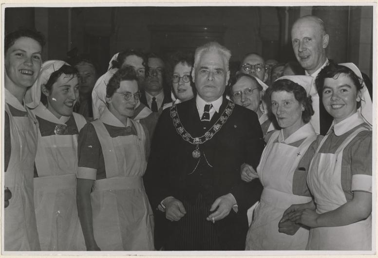11 april 1951: Burgemeester P.J. Oud omringd door verpleegkundigen tijdens de viering van het 40-jarig bestaan van de vereniging het Groene Kruis. Deze particuliere organisatie leverde een grote bijdrage aan de verbetering van de volksgezondheid in Rotterdam. Fotograaf Karel Adelmund. Collectie 4282, XXXIII-797-00-01-KL