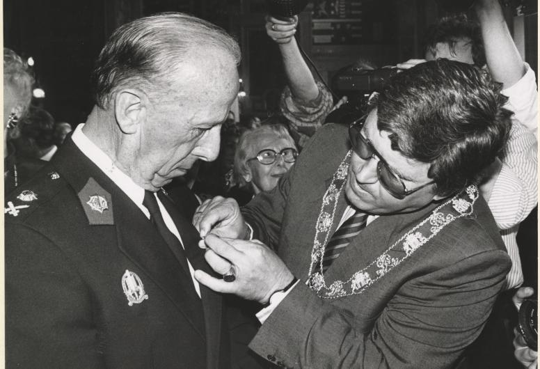 Hoofdcommissaris J.A. Blaauw krijgt tijdens zijn afscheid in het stadhuis door burgemeester Peper de versierselen opgespeld die behoren bij de orde van Ridder van de Nederlandse Leeuw. Collectie 4282, 1988-883-kl