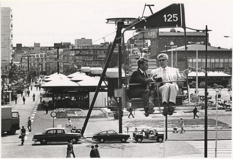 24 juni 1970: Journalist Han van der Meijde (Het Parool) interviewt burgemeester Thomassen in de kabelbaan die ter gelegenheid van de C70 is aangelegd door de binnenstad van Rotterdam. De kabelbaan had een lengte van 2 kilometer en hing over de Binnenweg, Karel Doormanstraat, Weena en Coolsingel. Via de manifestatie C70 wilde het Rotterdamse gemeentebestuur in ‘een gezellige en ongedwongen sfeer’ laten zien wat na 25 jaar bouwen tot stand was gekomen. Fotograaf Peter Molkenboer. Collectie 4282-1970-1700-KL