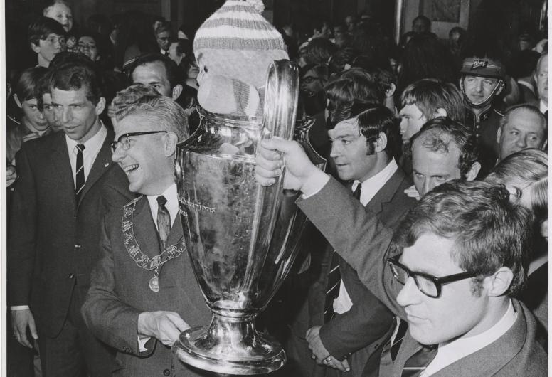 7 mei 1970: Rinus Israël aanvoerder van Feyenoord en burgemeester Thomassen presenteren trots de Europacup I.  Feyenoord is de eerste Nederlandse club die de Europacup I wist te winnen. In de finale versloegen zij, na verlenging, het Schotse Celtic met 2-1. In de cup zit de Celtic-mascotte, een gebreide pop van een halve meter hoog in de clubkleuren groen-wit, die de aanvoerder van de Schotse club cadeau had gedaan aan Feyenoord. Fotograaf Hans Vrijmoet. Collectie 4282, 1970-725-kl