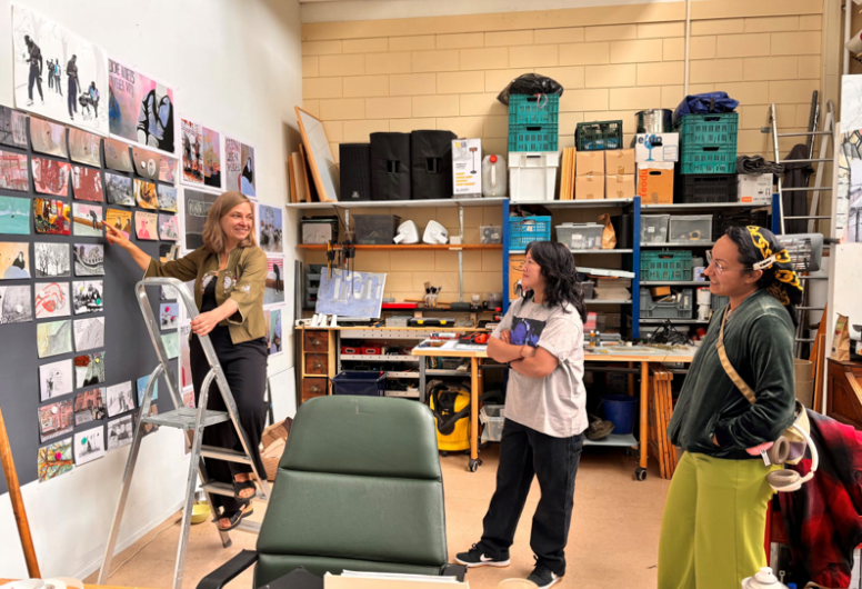 Christine Saarfeld toont haar collectie aan twee aanwezigen terwijl ze op een trapje staat