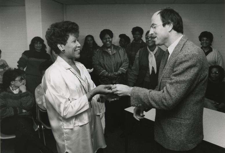 Zwart wit foto van een groep Surinaamse vrouwen en een Nederlandse man die een sleutel overhandigd
