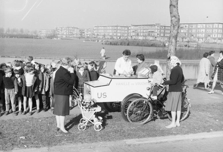 Kinderen staan in de rij bij een ijskraam ijsverkoper in het Vroesenpark aan de Stadhoudersweg. Rechtsachter zijn de huizen aan de Vroesenlaan te zien. 