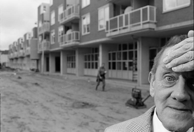 Een man staat met de hand op het hoofd voor nieuwbouwwoningen aan de Gaffelstraat. Op de voorgrond wordt de grond geëgaliseerd. De foto is gemaakt voor het boek 'Die stad komt nooit af'.