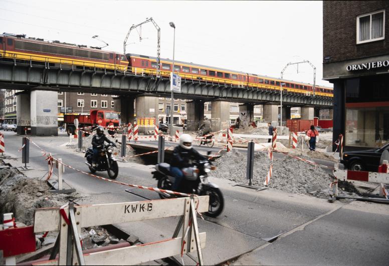 De Binnenrotte ligt open voor de aanleg van de Willemsspoortunnel. De foto is vanaf de kruising bij de Meent gemaakt. Boven de weg raast een trein voorbij over het luchtspoor. 5 april 1988.