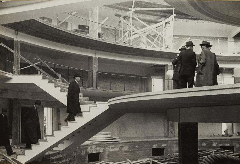 Een interieurfoto van het middengedeelte van het Bouwcentrum in aanbouw. Een aantal mannen bezichtigen het gebouw vanaf het middenstuk, 1948. Collectie 4100, nummer 2016-35-103