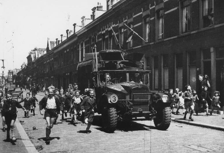 Een geallieerde militaire geluidswagen rijdt in een straat in de wijk Kralingen en wordt verwelkomd door de jeugd, 10-05-1945 - 30-05-1945.