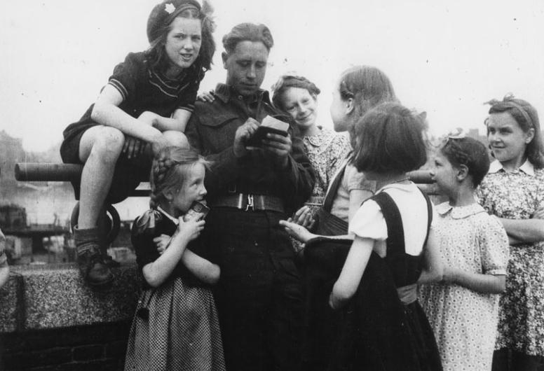 Een militair deelt handtekeningen uit aan meisjes [vermoedelijk aan de Boompjes bij de oprit naar de Willemsburg], 10-05-1945 - 30-05-1945.