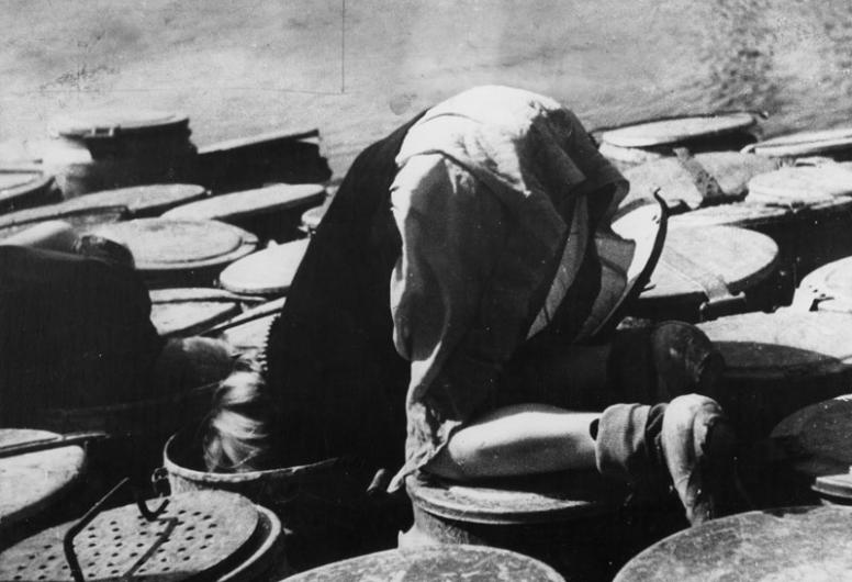 Een kind zoekt voedselresten in vuilnisbak tijdens de hongerwinter, 1944 - 1945.