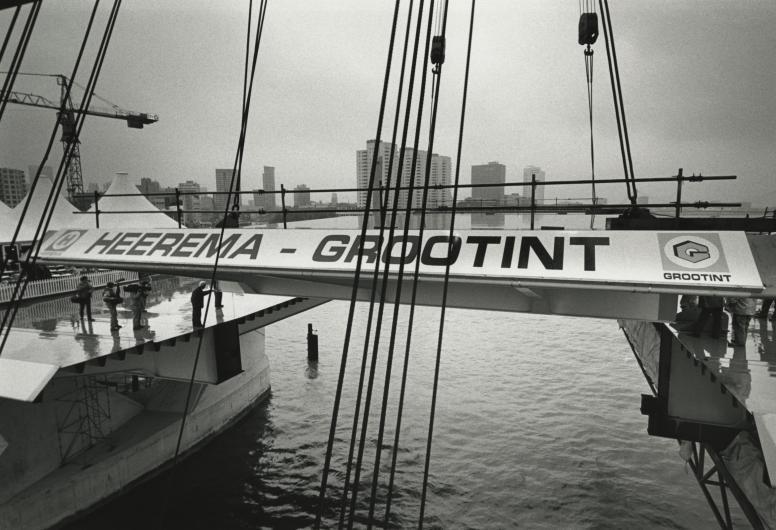 Fotografen zijn aanwezig bij het plaatsen van het laatste brugdeel van de Erasmusbrug. Aan het brugdeel hangt een bord met de namen van de firma's Heerema en Grootint. 1996. NL-RtSA_4110_1996-2269