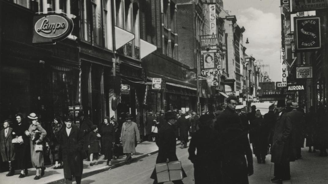 Hoogstraat bij de Wijde Kerksteeg, vanuit het westen, tussen Spui en Vlasmarkt. Op de voorgevel van bioscoop Thalia reclame voor een film van Shirley Temple, 1939.