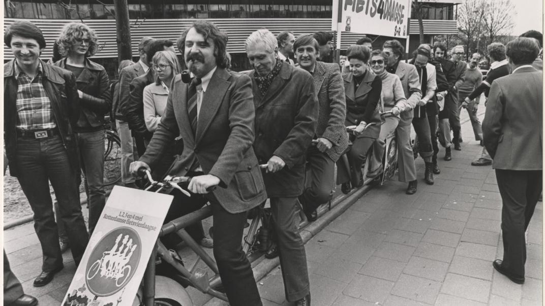 25 april 1978: Het College van Burgemeester en Wethouders maken reclame voor de Rotterdamse fietsvierdaagse op 1,2,3, en 4 mei 1978. Het gezelschap poseert op een elfpersoonsfiets voor het Gemeentelijk Rekencentrum aan de Stationssingel. Op de foto o.a. burgemeester André van der Louw, de wethouders J.G. van der Ploeg, Mentink, Schmitz, Van der Have, Riezenkamp, Mastik en Van der Pols. Foto: Rotterdams Nieuwsblad. Collectie 4282, 1978-1370-kl