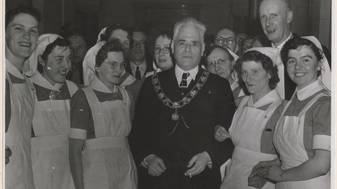 11 april 1951: Burgemeester P.J. Oud omringd door verpleegkundigen tijdens de viering van het 40-jarig bestaan van de vereniging het Groene Kruis. Deze particuliere organisatie leverde een grote bijdrage aan de verbetering van de volksgezondheid in Rotterdam. Fotograaf Karel Adelmund. Collectie 4282, XXXIII-797-00-01-KL